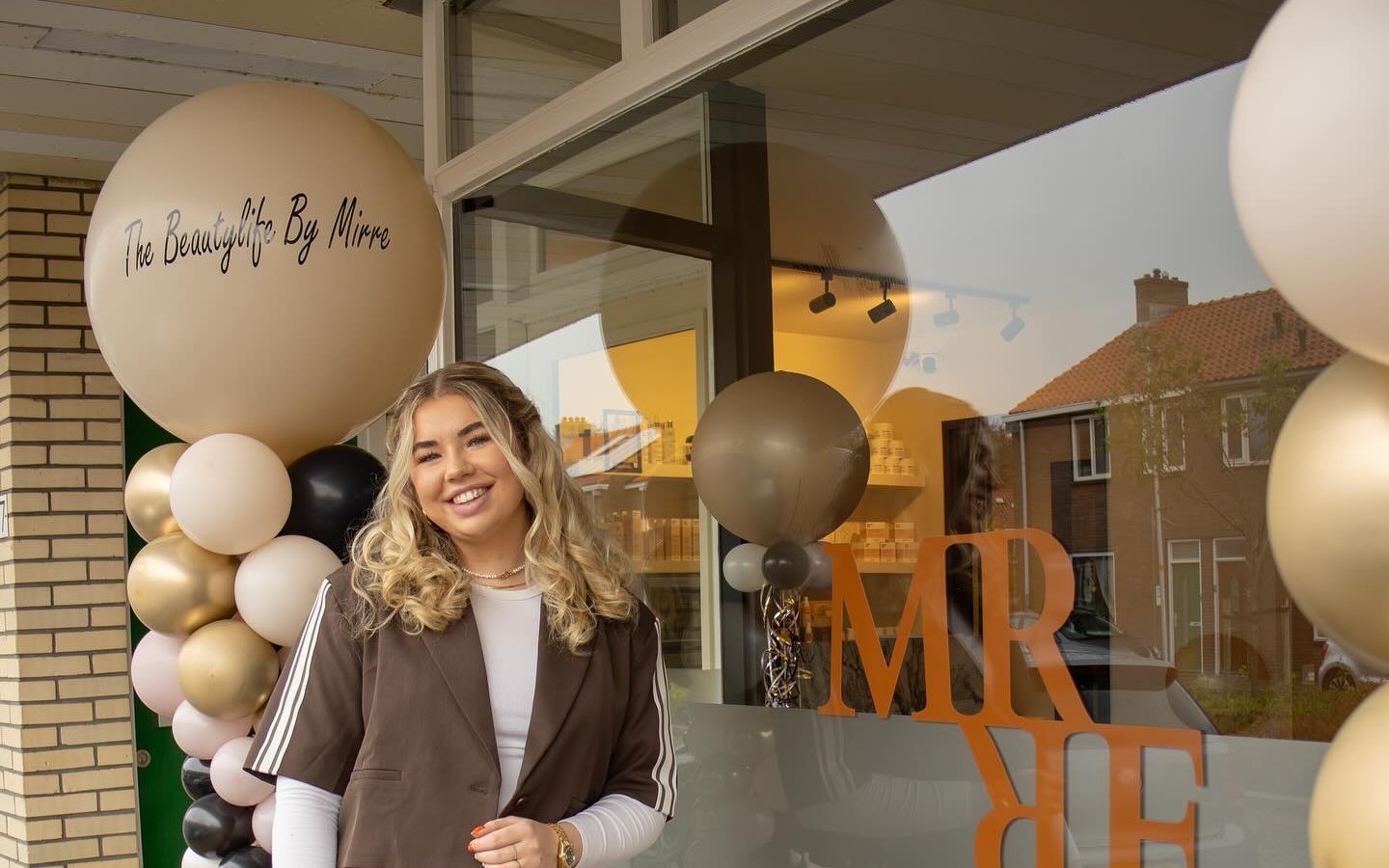 Mirre voor het raam van haar salon aan de Ieplaan, met het logo op de ruit